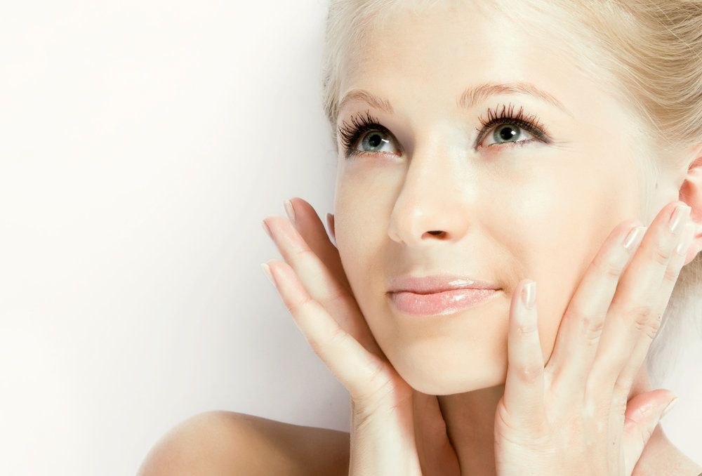 Young woman against a white background, looking up with hands to face